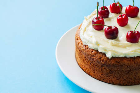 Homemade sour cream cake with cream cheese frosting decorated with fresh ripe cherries on a light blue background. Close up and copy space.の写真素材