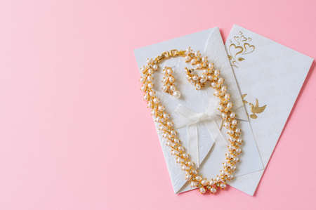 Wedding concept. Invitation cars and pearl necklace on a pink background.の写真素材