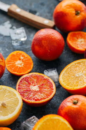 Mix of fresh ripe citrus fruits. Blood oranges, mandarines, lemons  with ice cubes on a blue stone background. Top view.の写真素材