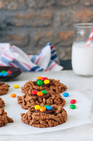Chocolate cookies with colorful smarties on a baking paper with galss of milk.