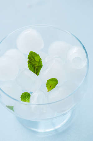Ice cubes in a glass bowl with mint leaves. Blue background.の写真素材