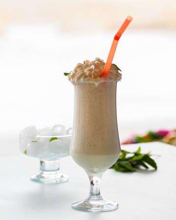 Banana and vanilla milkshake with whipped cream and straw in a tall glass.の写真素材