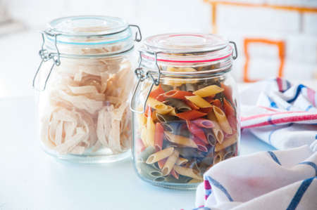 Uncooked colored penne and tagliatelle pasta in a jar. Close up.