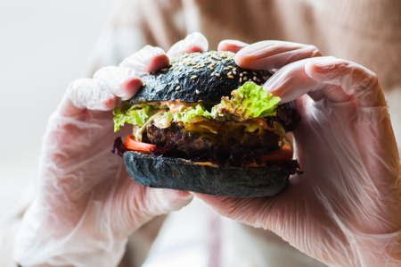 Black burger in a hands of hipster. Close up. Fast or junk food concept.の写真素材