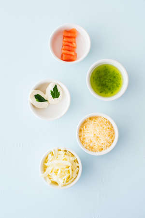 Food ingredients for pizza in a small bowls on a blue background. Minced parmesan and mozzarella,...