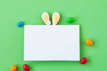 Easter background concept. Easter bunny ears under white empty paper on green background.の写真素材