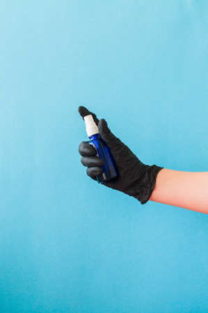 Hand with black gloves holding sanitizer. Blue background. Safety or health protection concept.