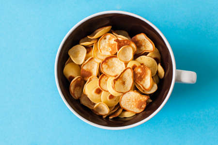 Homemade vanilla tiny pancake cereal in a bowl. Blue background. Top view.