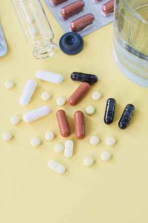 Various tablets and pills on yellow background. Top view.