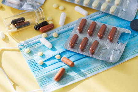 Various tablets, pills, blue medical mask on yellow background. Health care concept.