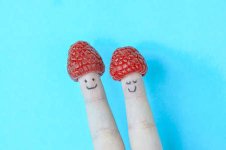 Two fingers with smiles and raspberry as a hat. blue background.