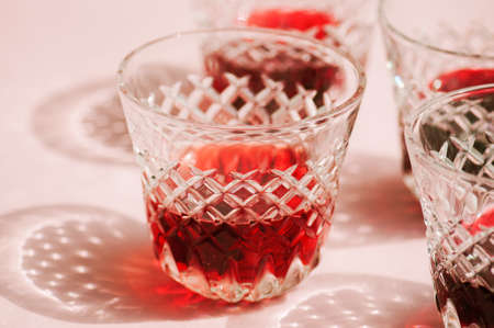 Red wine in a transparent glass with abstract shadows on pink background.の写真素材