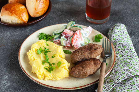 Homemade meat cutlets with mached potatoes and vegetable salad in a plate on a gray background.