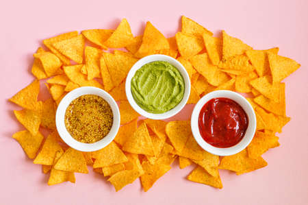 Heap of corn tortilla chips with french mustard , guacamole and ketchup on a pink background. Top ivew.の写真素材