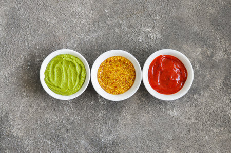 Three types of sauces, french mustard, ketchup and guacamole on a gray background.の写真素材