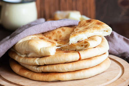 Popular Ossetian khachapuri pies stuffed with potato and cheese, whole and sliced on a wooden board...