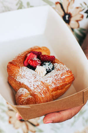 Perfect danish puff pastry with cream and berries in a craft paper box in a hand. Take away food...