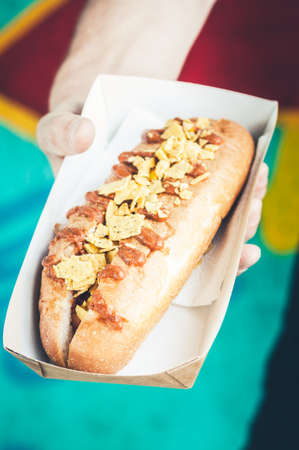 Freshly prepared hotdog with salsa and fried onions in a paper box in a hand. food delivery concept. green background.の写真素材