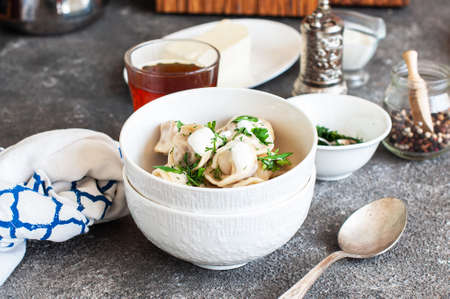 Homemade Meat Dumplings - Russian traditional pelmeni stuffed with minced beef meat served in a white bowl with sour cream and greens on a gray background.の写真素材