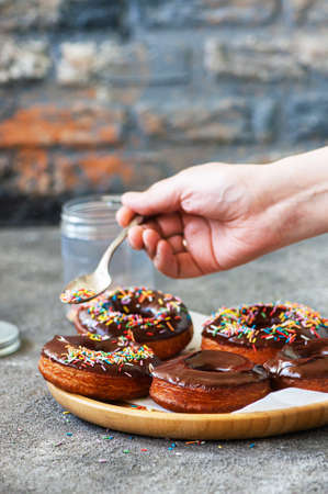 Fried donuts with chocolate glaze. Woman's hand decorating donuts with colorful sprinkles.の写真素材