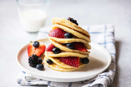 Close up of vanilla pancakes with fruits and berries and galss of milk on a gray background.の写真素材