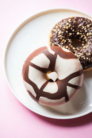 Two donuts with chocolate glaze served on a white plate on a pink background. Close up.の写真素材