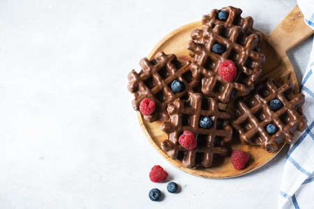 Chocolate waffles and berries on a wooden plate on a wooden background. Top view and copy space.