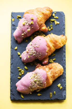 Mini-croissants with ruby chocolate and pistachios on a slate board. Overhead view.の写真素材