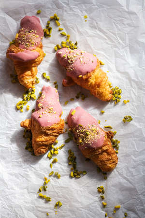 Mini-croissants with ruby chocolate and pistachios on a baking paper. Overhead view.の写真素材