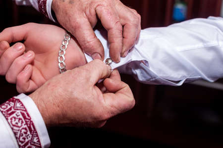 Man fastens cufflink on the grooms sleeve