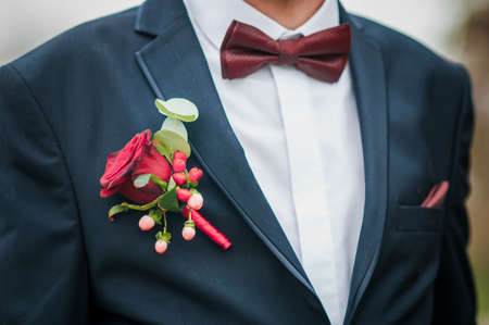 Dark red bowtie on grooms neck and red rose on the jacketの写真素材