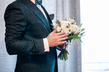 Groom holding white bouquet of roses in the handsの写真素材