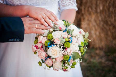 Hands of groom and bride lie on the bouquet of flowersの写真素材