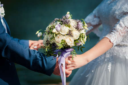Bride and groom hands with flower bouquet in the hands