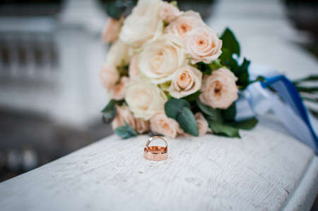pair of gold wedding rings on the white marble with flowersの写真素材