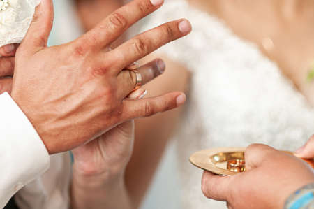Bride wearing gold wedding ring on the finger of groomの写真素材