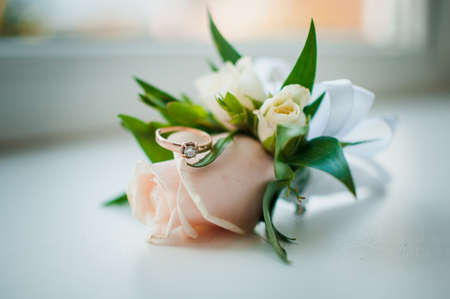 White and pink rose boutonniere and gold ring with gem on the white background