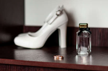 Three gold wedding rings and white high heel shoe on the tableの写真素材