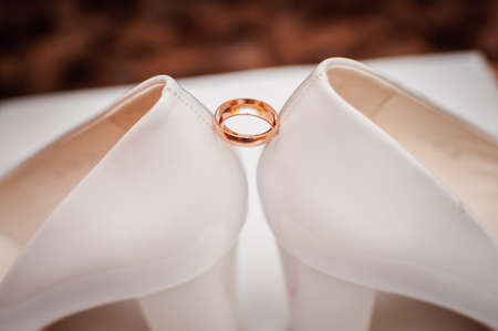 Pair of golden wedding rings between pair of a white shoesの写真素材