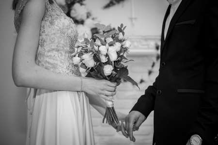 A bouquet of white flowers in the hands of the bride. The groom holds the bride in his handの写真素材