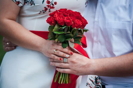 the newlyweds are holding a bouquet with red rosesの写真素材