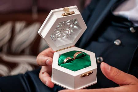 the groom holds wedding rings in a white box
