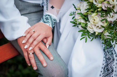 hands of newlyweds with wedding rings and wedding bouquetの写真素材