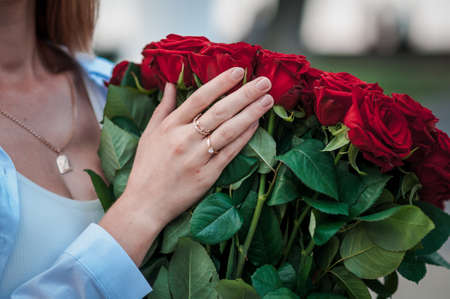 guy holds the girl's hand with a wedding ring over a bouquet of red rosesの写真素材