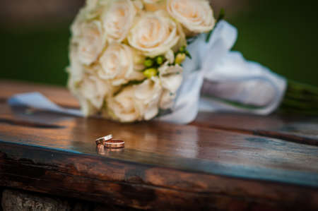 Wedding rings on a wooden stand against the background of the bride's bouquetの写真素材
