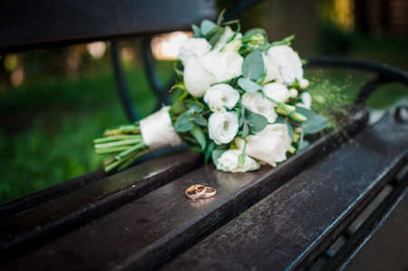 Wedding rings on a wooden stand against the background of the bride's bouquetの写真素材