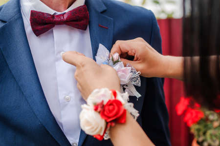 Boutonniere of the groom with white flowers in the hands of the bride