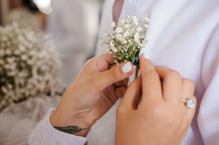 Boutonniere of the groom with white flowers in the hands of the bride
