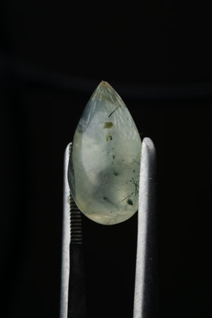Natural prehnite stone in tweezers on a black background
