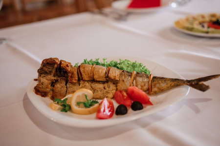 Baked fish with vegetables. Lemon, tomato, olives, lettuce, parsley. Festive tableの写真素材